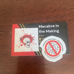 Op de afbeelding: Een witte sticker met een rode cirkel en een zwart symbool van een brein met een diagonale lijn erdoorheen. De tekst "RAGING AGAINST THE MACHINE" staat in een rode cirkel rond het symbool. De tekst "CREATIVES AGAINST AI" staat in een zwarte cirkel onder het symbool.