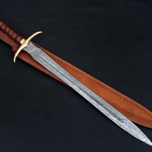 May include: A long, silver sword with a leather scabbard. The sword has a gold-colored hilt and a decorative pattern on the blade.