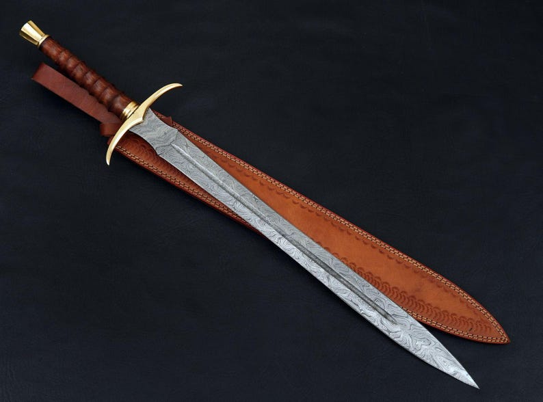 May include: A long, silver sword with a leather scabbard. The sword has a gold-colored hilt and a decorative pattern on the blade.