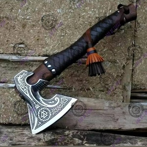 May include: A handcrafted axe with a silver blade featuring intricate Celtic knotwork. The wooden handle is wrapped in dark brown leather with decorative stitching and a tassel. The axe head is approximately 6 inches wide.