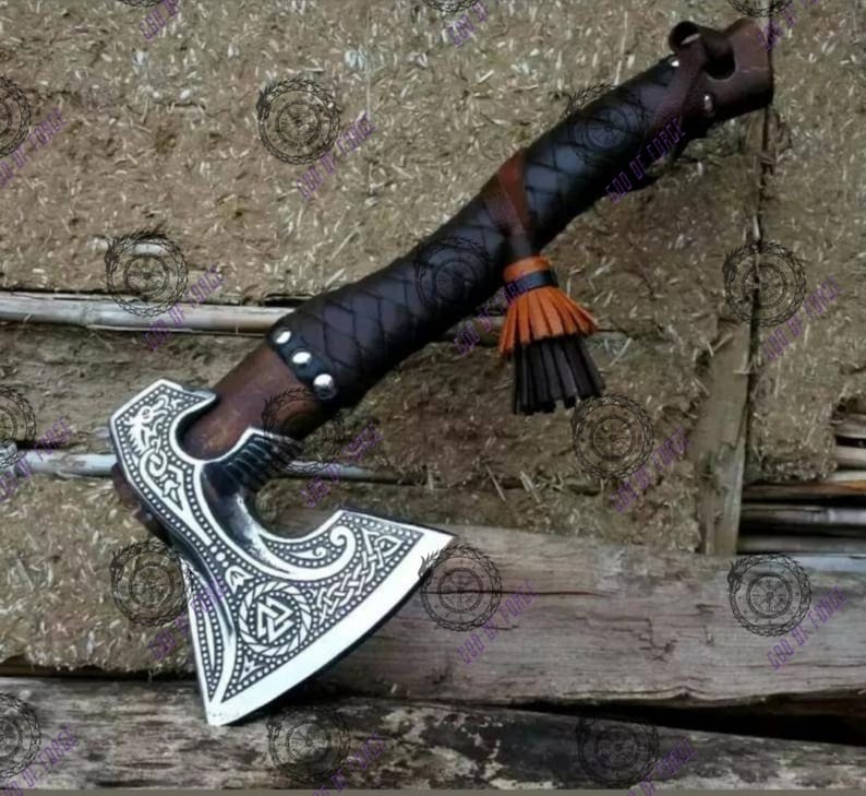 May include: A handcrafted axe with a silver blade featuring intricate Celtic knotwork. The wooden handle is wrapped in dark brown leather with decorative stitching and a tassel. The axe head is approximately 6 inches wide.