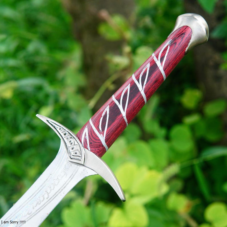 May include: A silver and red sword with a wooden handle and a silver blade. The blade has an inscription on it. The sword is a replica of a fantasy sword.