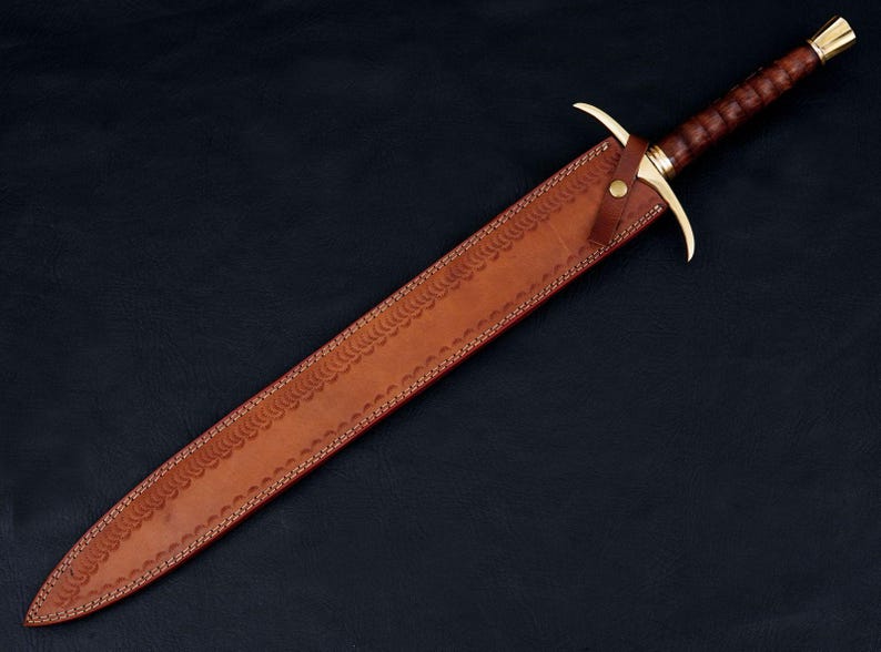 May include: A brown leather scabbard with a decorative pattern and a gold-colored metal tip. The scabbard is for a sword with a brown leather wrapped handle and a gold-colored metal pommel.