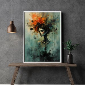 Op de afbeelding: Een ingelijste kunstdruk met een portret van een vrouw in abstracte stijl. Het kunstwerk gebruikt tinten teal, oranje en zwart, met de focus op het gezicht en bovenlichaam van de vrouw. De print wordt gepresenteerd op een houten tafel.