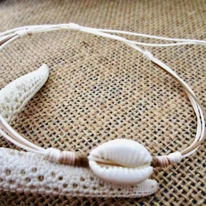 May include: A seashell anklet in white and tan. The anklet has a natural seashell as its focal point, strung on a thin, adjustable cord. The anklet is shown on a white starfish against a textured, tan background.