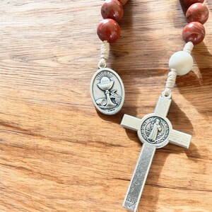 May include: A brown wooden rosary with a silver chalice pendant and a silver cross with a Saint Anthony of Padua medal. The cross has the words "Ora Pro Nobis" and "Sanctus Antonius" on it.
