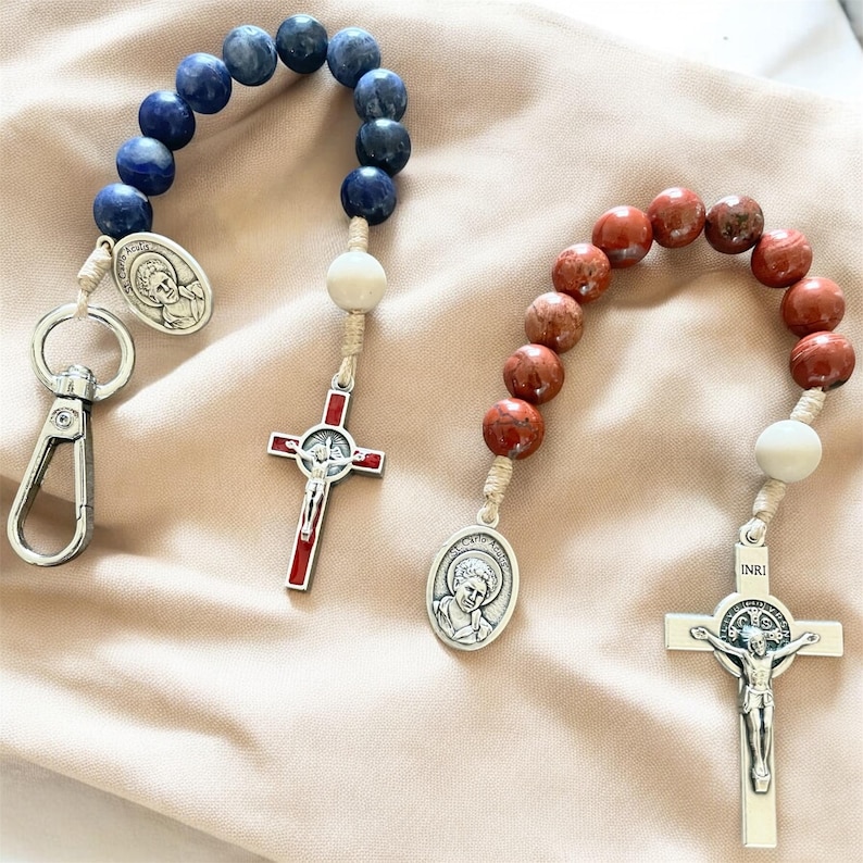 May include: Two beaded rosaries with silver crucifixes and medallions. One rosary has blue beads and the other has red beads.