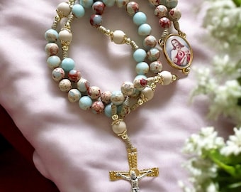 May include: A blue and white rosary with a gold cross and a gold medallion featuring a depiction of Jesus Christ. The rosary is made of small, round beads and is strung on a cord.