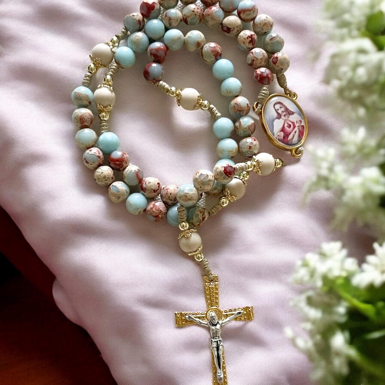 May include: A blue and white rosary with a gold cross and a gold medallion featuring a depiction of Jesus Christ. The rosary is made of small, round beads and is strung on a cord.