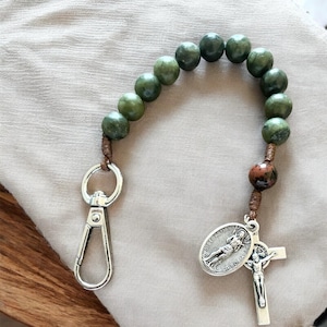 May include: A green stone rosary with a brown leather cord and a silver charm. The rosary has a silver clasp and a silver cross charm.