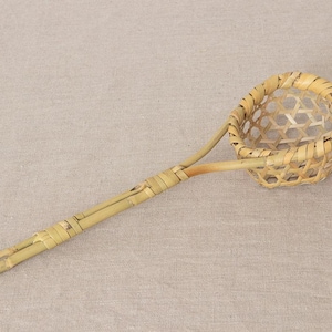 May include: A handcrafted bamboo scoop with a woven basket-like bowl. The scoop features a long handle and a rounded bowl, perfect for serving or straining. The natural bamboo color and intricate weave create a rustic aesthetic.