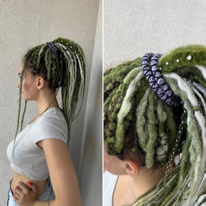 K&ouml;nnte beinhalten: Zwei Frauen mit langen gr&uuml;nen und wei&szlig;en Dreadlocks. Eine Frau tr&auml;gt ein lila-wei&szlig;es Perlenhaarband. Die andere Frau tr&auml;gt ein wei&szlig;es Crop-Top.