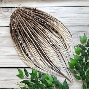 Könnte beinhalten: Braune und weiße synthetische Dreadlocks mit Perlen und Schnurakzente. Die Dreadlocks sind fächerförmig angeordnet und liegen auf einer Holzoberfläche.