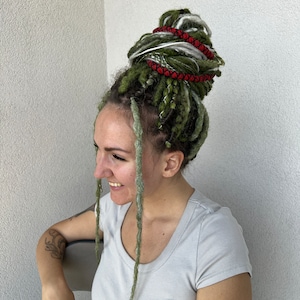 K&ouml;nnte beinhalten: Eine Person mit gr&uuml;nen, wei&szlig;en und roten Dreadlocks, die zu einem Dutt gebunden sind. Die Dreadlocks sind mit roter Schnur und einem silbernen Ring gebunden.