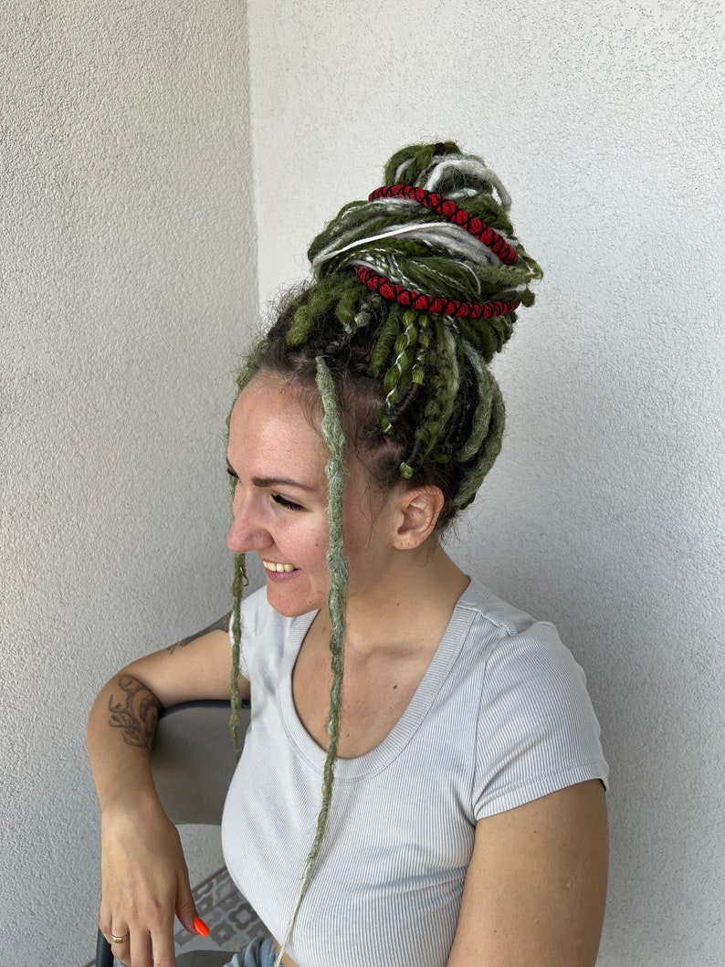 K&ouml;nnte beinhalten: Eine Person mit gr&uuml;nen, wei&szlig;en und roten Dreadlocks, die zu einem Dutt gebunden sind. Die Dreadlocks sind mit roter Schnur und einem silbernen Ring gebunden.