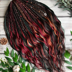May include: A set of colorful dreadlocks with a mix of dark brown, red, green, and orange hues. The dreadlocks are styled with braids and wavy ends, and adorned with small beads. The hair is arranged on a wooden surface with green leaves and pinecones.