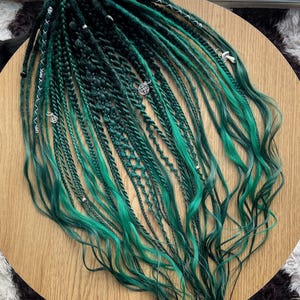 May include: Green and black synthetic dreadlocks with silver beads and charms. The dreadlocks are long and wavy.