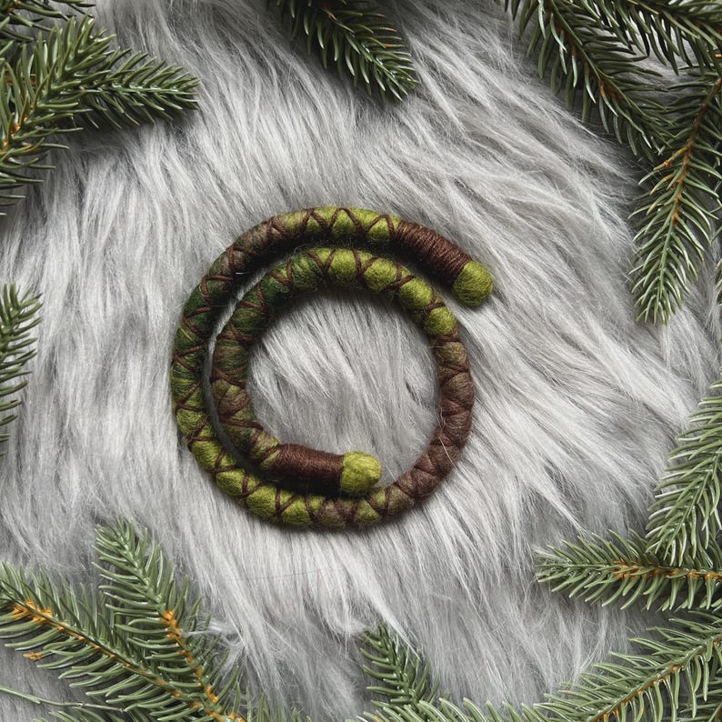 K&ouml;nnte beinhalten: Ein gr&uuml;ner und brauner Woll-Haarwickel, auch bekannt als Dreadlock-Wickel, auf einem grauen, flauschigen Hintergrund.
