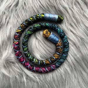 May include: A colourful braided cord with a black background and pink, yellow, green, and blue accents. The cord is coiled into a circle.