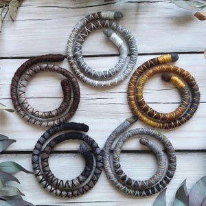 May include: Five different colored coiled cords made of yarn. The cords are in a circular shape and are arranged in a circle on a white wooden surface.