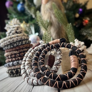 Op de afbeelding: Een set van vier handgemaakte macramé koordsarmbandjes in zwart, wit, bruin en beige. De armbandjes zijn in een cirkelvormig patroon met elkaar verweven.