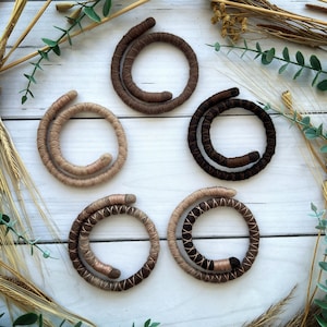 Op de afbeelding: Vijf handgemaakte gewikkelde touw armbanden in verschillende bruintinten. De armbanden zijn in een cirkel op een wit houten oppervlak gerangschikt.