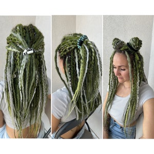 K&ouml;nnte beinhalten: Gr&uuml;ne und wei&szlig;e synthetische Dreadlocks mit schwarzen und wei&szlig;en Haarklammern. Die Dreadlocks sind auf verschiedene Arten gestylt, darunter ein Pferdeschwanz, zwei Dutt und locker.