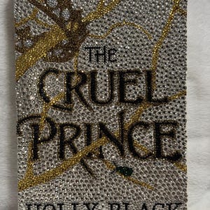 Pu&ograve; includere: Una copertina di libro con un design argento, oro e nero. Il titolo "The Cruel Prince" &egrave; scritto in lettere nere. L'autore "Holly Black" &egrave; scritto in lettere nere nella parte inferiore della copertina.