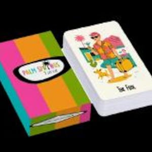 Peut inclure: Un jeu de cartes et son &eacute;tui. La bo&icirc;te pr&eacute;sente des rayures verticales roses, oranges, vertes et jaunes. Le texte "Palm Springs" est dans un ovale noir. Les cartes montrent un personnage de dessin anim&eacute; avec un chien, des palmiers et le texte "Eat Fast".