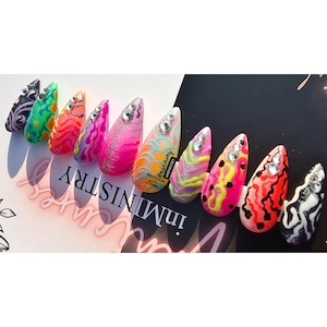May include: A set of ten almond-shaped press-on nails featuring vibrant, multi-colored abstract patterns, swirls, and glitter accents. Each nail is embellished with clear rhinestones and one nail displays the text Manicures inMINISTRY.
