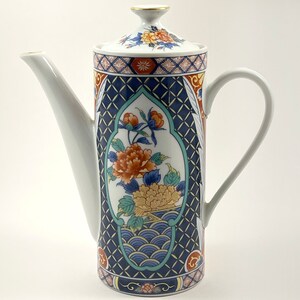 May include: A white ceramic coffee pot with a blue, green, and gold floral design. The pot has a lid and a handle.