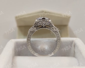 May include: A silver engagement ring with a large, round, clear center stone and smaller stones set in a delicate, ornate design. The ring is in a white box.