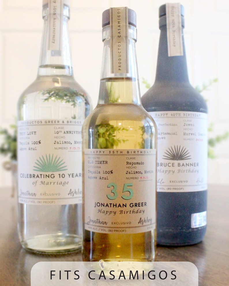 K&ouml;nnte beinhalten: Drei Flaschen Tequila mit personalisierten Etiketten. Die Etiketten sind wei&szlig; mit schwarzem Text und einem gr&uuml;nen Agavenpflanzendesign. Die Etiketten feiern ein 10-j&auml;hriges Hochzeitsjubil&auml;um, einen 35. Geburtstag und einen 40. Geburtstag. Die Flaschen sind mit "Fits Casamigos" gekennzeichnet.