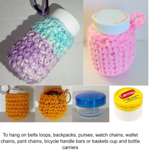 Könnte beinhalten: Gehäkelte Flaschen- und Glasbehälterträger in Pink, Lila, Blau und Orange. Die Träger haben eine Schlaufe zum Aufhängen an Gürteln, Rucksäcken, Handtaschen, Uhrenketten, Geldbörsenketten, Hosentaschenketten, Fahrradlenkern oder Körben. Das Bild zeigt auch eine Tube Carmex Lippenbalsam.