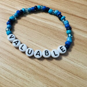 May include: A blue and white beaded bracelet with the word "VALUABLE" spelled out in white beads.