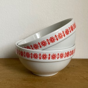 May include: Three white ceramic bowls with a red floral pattern around the rim. The bowls are stacked on top of each other.