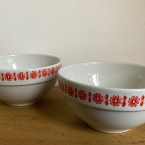 May include: Two white ceramic bowls with a red floral pattern around the rim.
