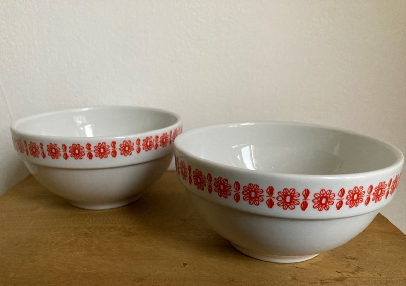 May include: Two white ceramic bowls with a red floral pattern around the rim.