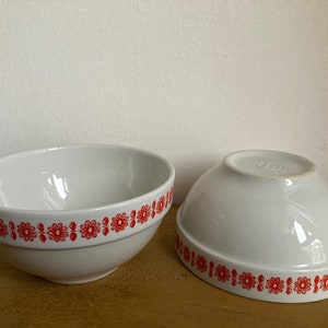 May include: Two white ceramic bowls with a red floral pattern around the rim. The bowls are empty and sitting on a wooden surface.