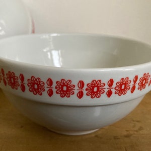 May include: White ceramic bowl with a red floral pattern around the rim. The bowl is empty and sitting on a wooden surface.