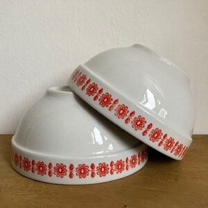 May include: Two white ceramic bowls with red floral designs around the rim. The bowls are stacked on top of each other.