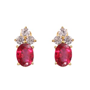 May include: A pair of gold earrings with a red oval gemstone surrounded by smaller clear gemstones.