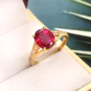 May include: A gold ring featuring a large, oval ruby gemstone set with smaller, clear gemstones.