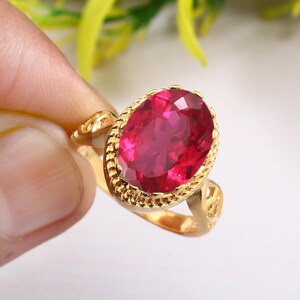 Peut inclure: Une bague en or avec une grande pierre précieuse rouge de forme ovale sertie dans un décor en or.