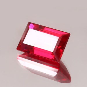May include: A deep red rectangular gemstone with a faceted cut.