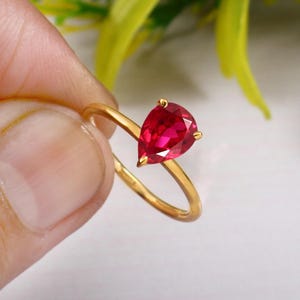 Könnte beinhalten: Ein goldener Ring mit einem tropfenförmigen Rubin.