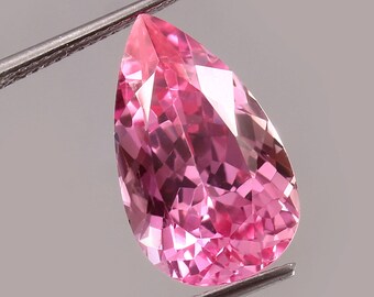 May include: A pear-shaped pink gemstone with a faceted cut. The gemstone is held by a pair of tweezers.