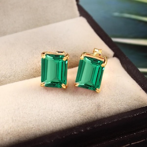 May include: A pair of gold earrings with emerald green square-shaped gemstones.