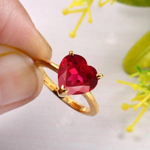 Puede incluir: Un anillo de oro con una gran piedra preciosa de rubí en forma de corazón.