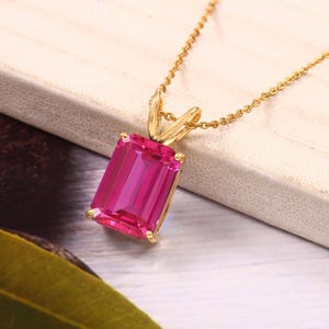 May include: A gold chain necklace with a pink emerald-cut gemstone pendant.